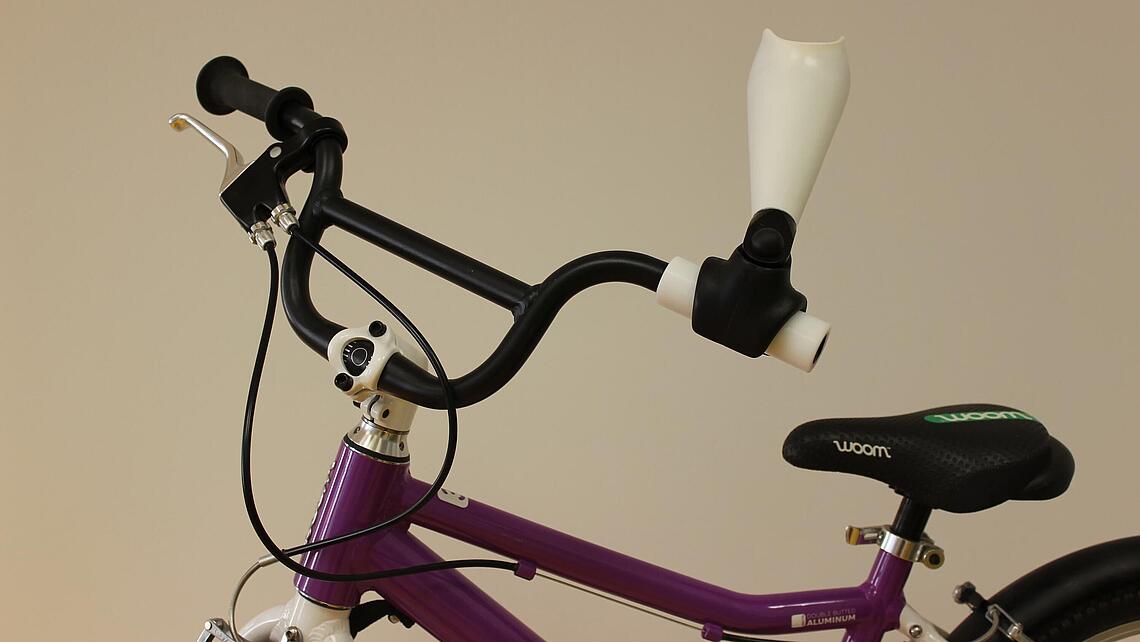 Adapter für Fahrradlenker, Kinderversorgung Unterarmprothese mit Adapter für einen Fahrradlenker an einem lila Kinderfahrrad
