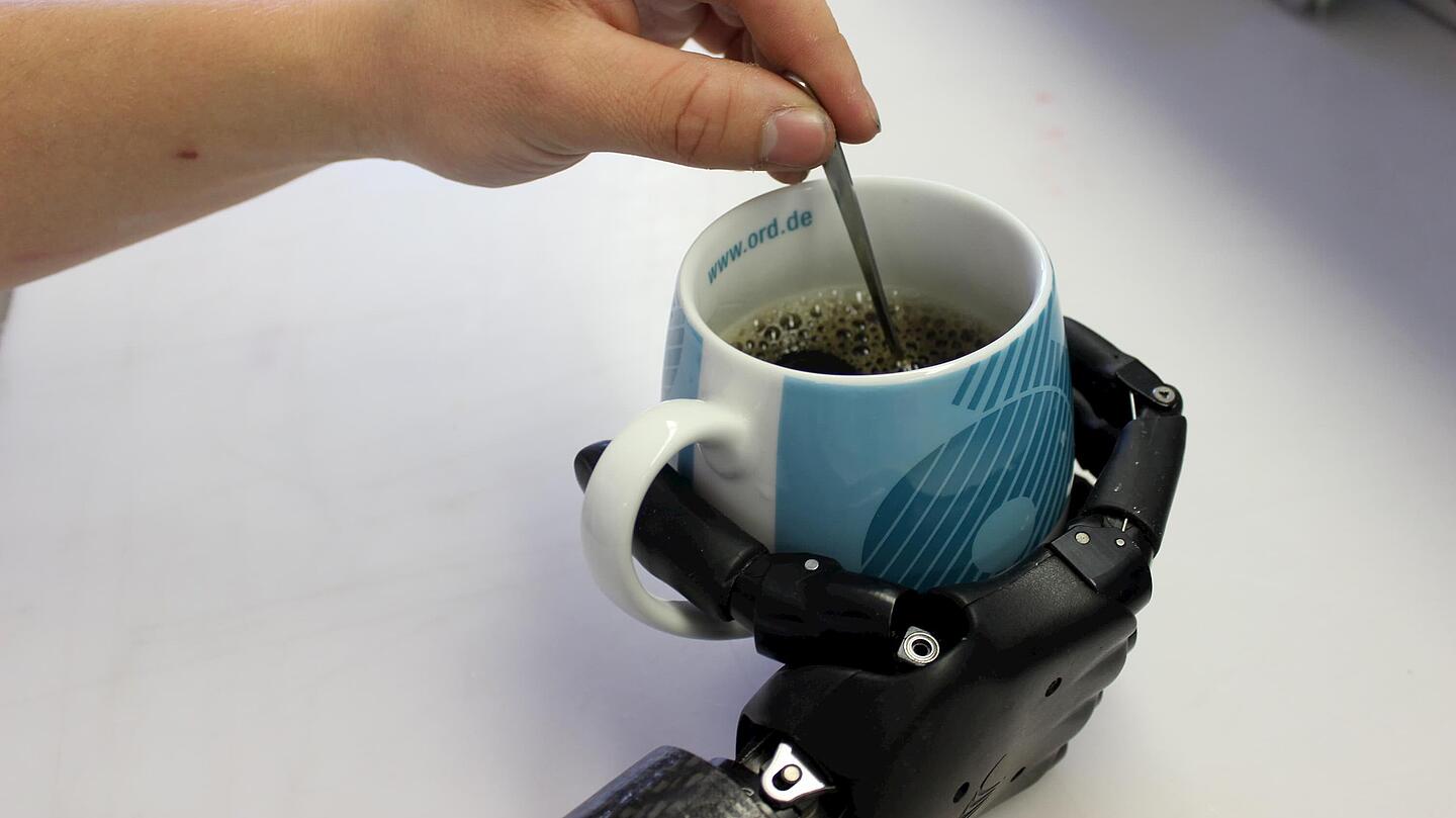 Unterarmprothese mit Kaffetasse Unterarmprothese mit Hand, die eine Kaffetasse hält
