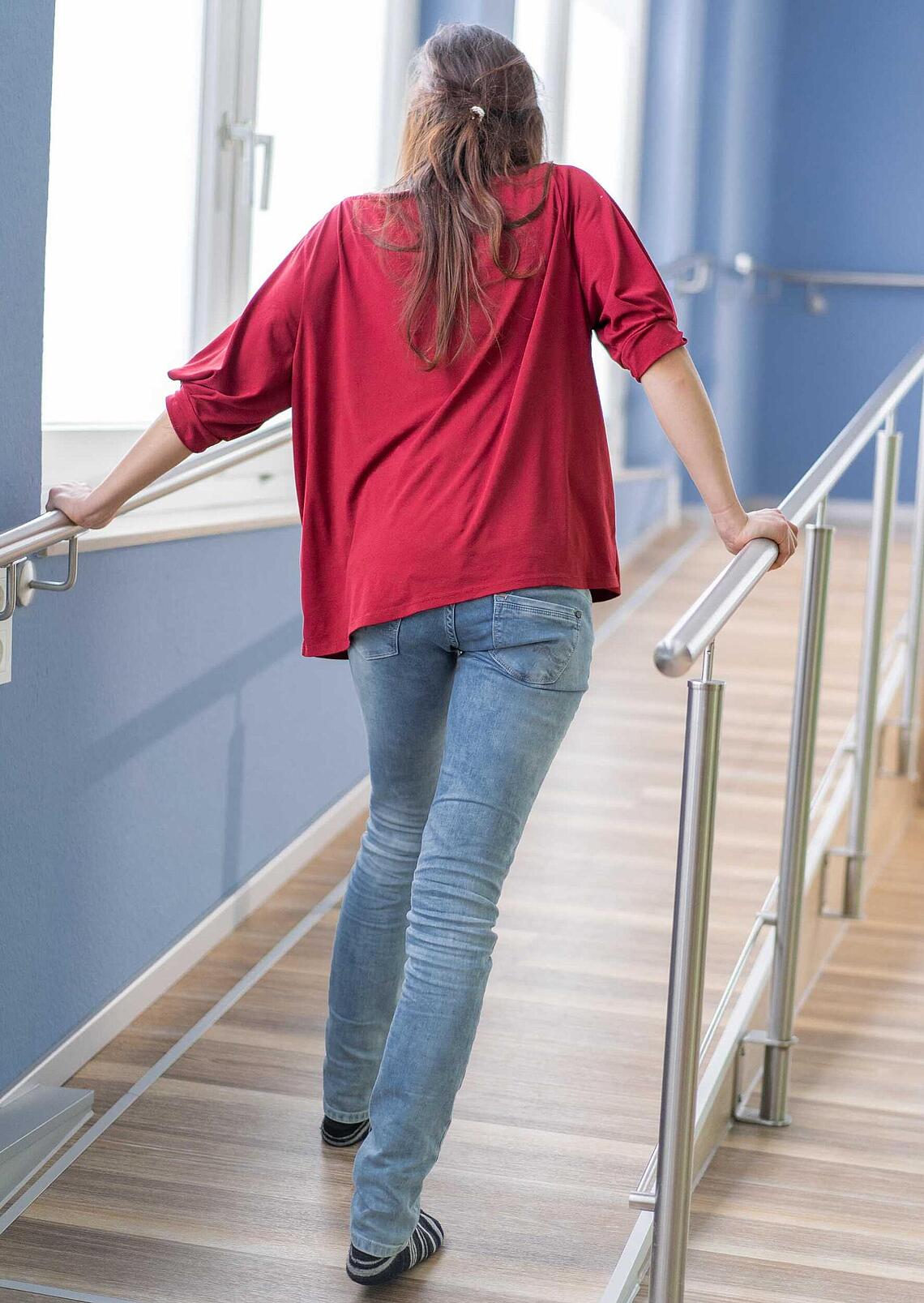 Frau mit Spastik geht Rampe hoch, © Ottobock Frau läuft ohne EXOPULSE Mollii Suit eine Rampe mühevoll hoch, © Ottobock