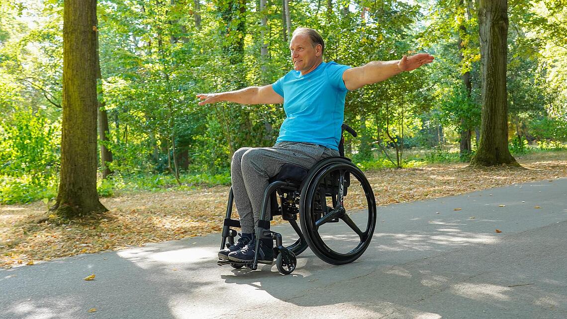 Rollstuhlfahrer im Park Mann im Rollstuhl fährt im Park und streckt Arme zum Test aus