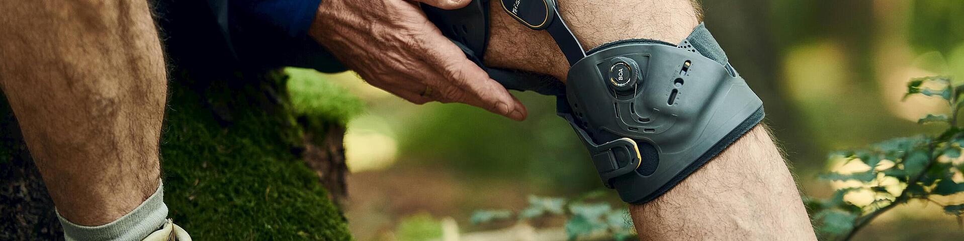 Orthese Unloader One X von Össur am Knie, © Copyrights by Össur hf Knie-Orthese Unloader One X von Össur beim Sitzen auf einem Baumstumpf während einer Waldwanderung, © Copyrights by Össur hf