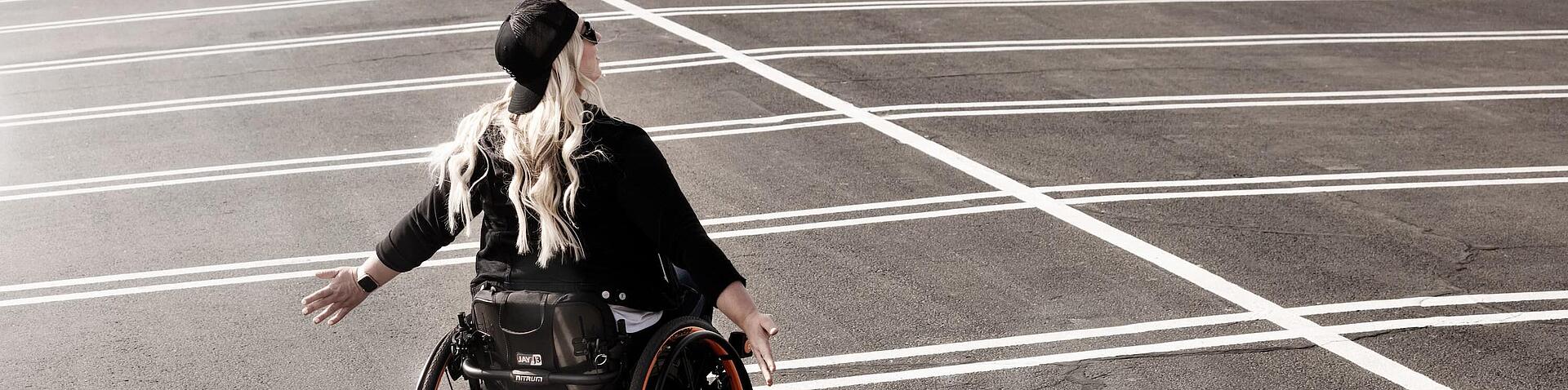 Frau im Rollstuhl auf leerem Parkplatz, Bildquelle: 2025, Sunrise Medical GmbH, Malsch/HD Frau im Rollstuhl steht auf leerem Parkplatz und hält die Arme zur Seite, Bildquelle: 2025, Sunrise Medical GmbH, Malsch/HD