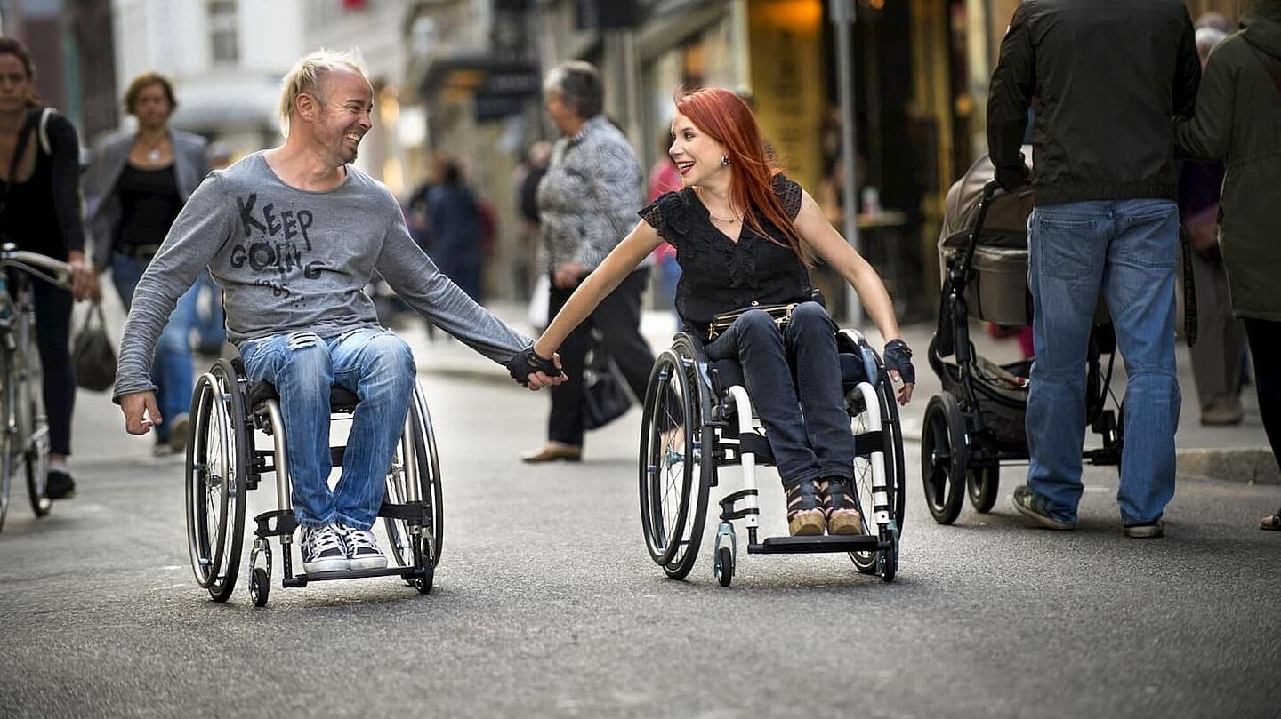 glückliches Paar die händehaltend im Rollstuhl sitzen, ©Invacare glückliches Paar aus Mann und Frau, die händehaltend im Rollstuhl sitzen, ©Invacare