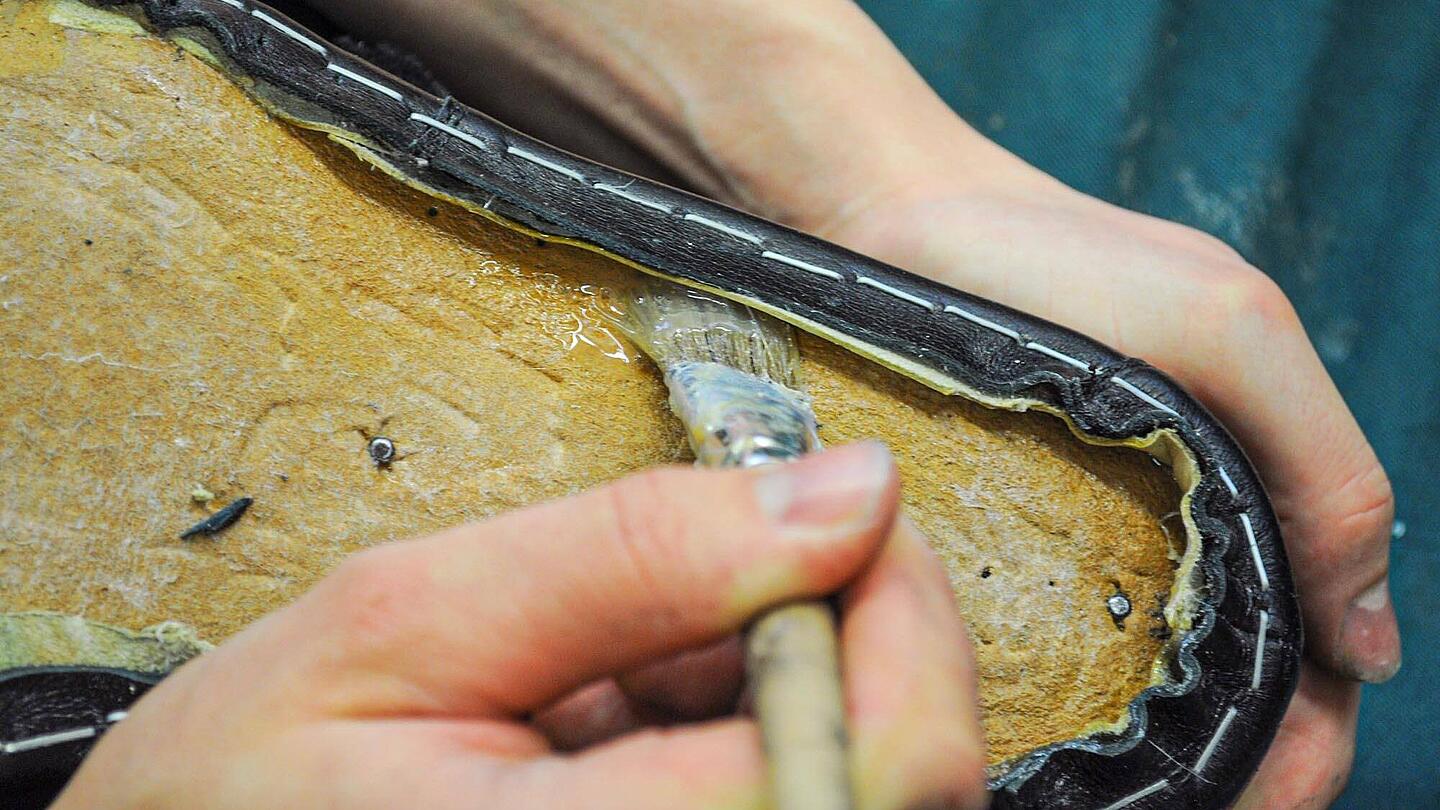 Ein Pinsel streicht Leim zwischen Schuhsole und Obermaterial Schuhsohle wird verleimt