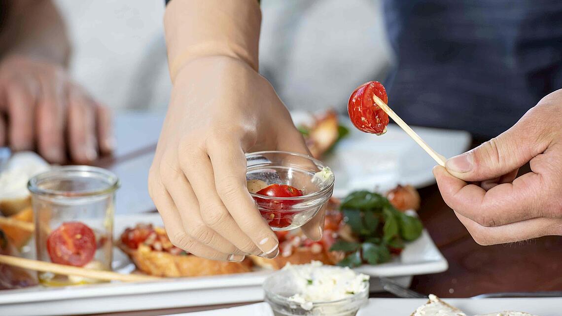 MyoPlus-Armprothese mit kleiner Glasschale mit Essen, © Ottobock MyoPlus-Armprothese, die eine kleine Glasschale mit Essen am Buffet hält, © Ottobock