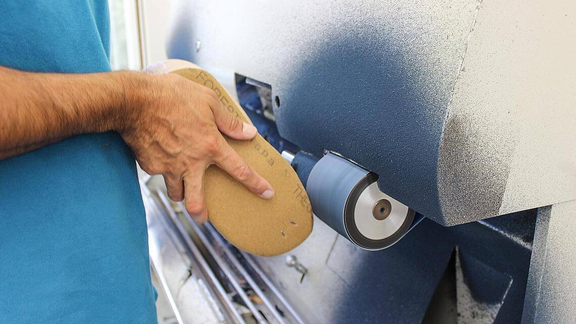 ein Mitarbeiter schleift eine Schuhleiste an einem Bandschleifer zu Schuhleiste wird an Bandschleifer zugeschliffen
