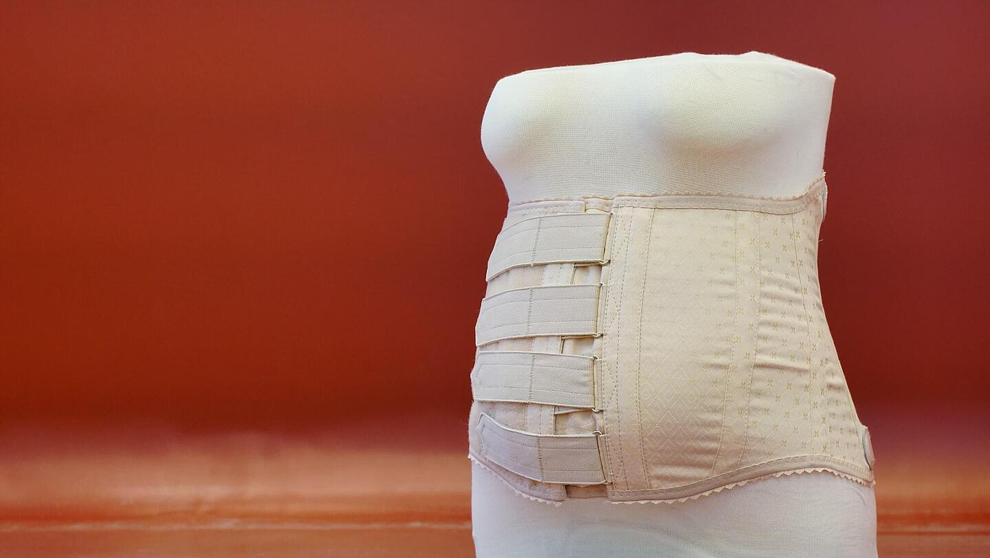 Vorderansicht eines Stützmieders nach Schanz Vorderansicht eines Stützmieders nach Schanz mit vertikal verlaufenden Metallverstärkungsstäben vor rotem Hintergrund